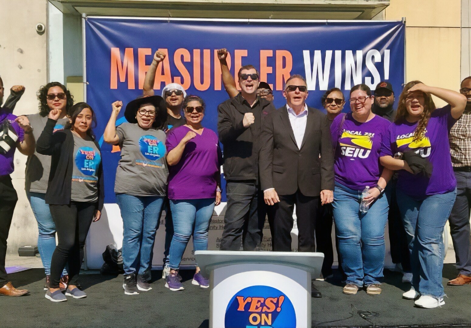 David Green and SEIU 721 members celebrating in front of a Measure ER Wins! banner with raised fists, gathered around a Yes On ER podium