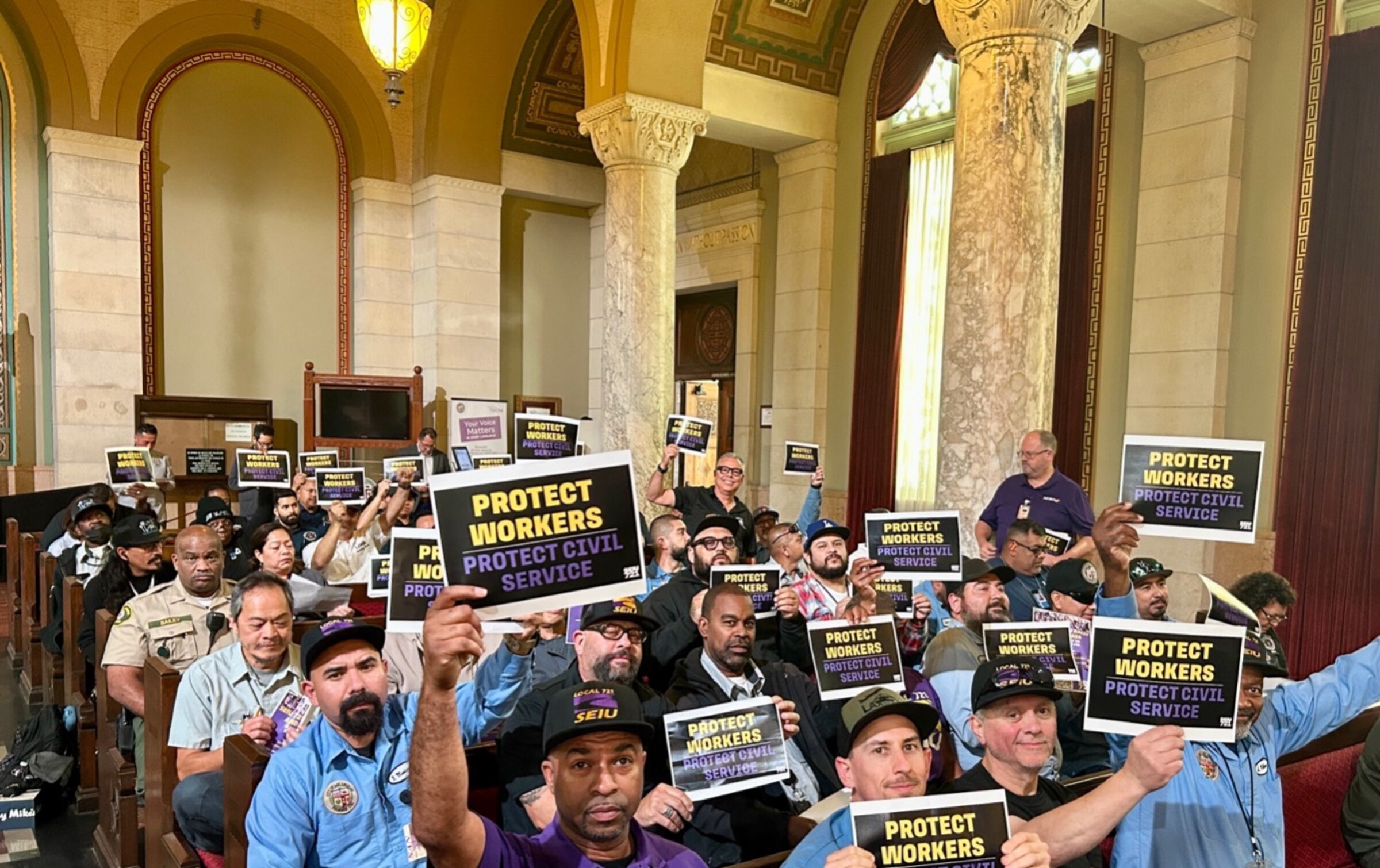 SEIU 721 coalition members in LA City Hall chambers holding Protect Workers, Protect Civil Service signs