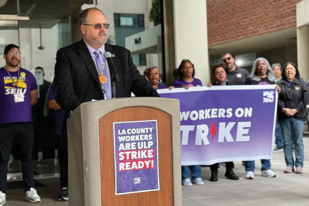 A union official addresses the media during a press conference as union members support him in the background.