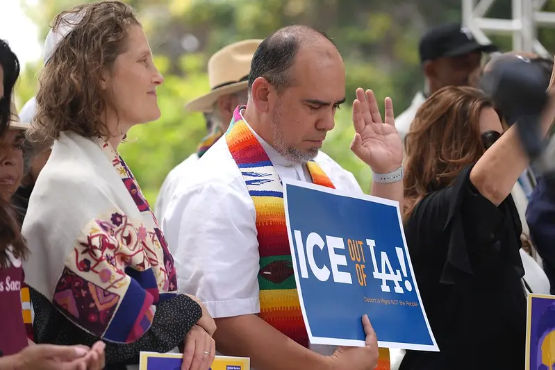 A clergyman holds a sign saying "ICE out of LA" at a union rally.