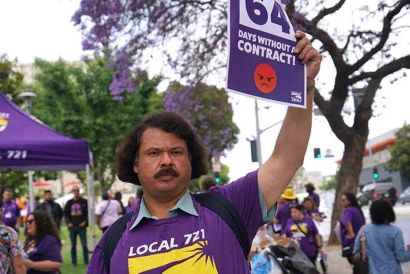 An SEIU 721 member holds aloft a sign indicating that LA County members have been working for 64 days without a contract.