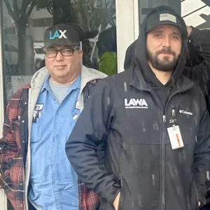 LAWA workers in uniform. The workers are both wearing baseball caps standing in front of LAWA headquarters.